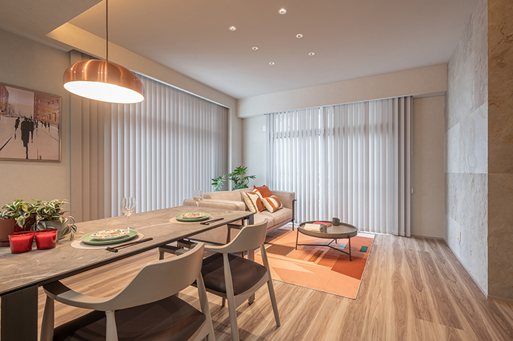 Open-plan dining and living room with a long wooden table, white chairs, beige sofa, and an orange rug.