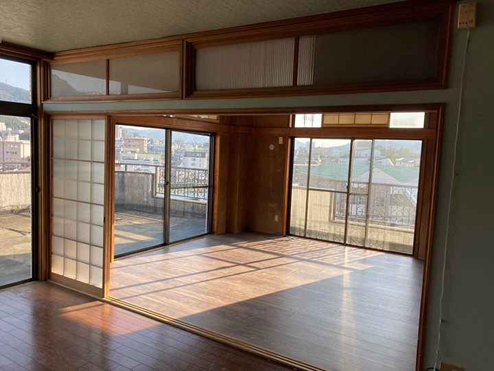 Empty living room with wooden floors and large sliding glass doors opening to a balcony, letting in sunlight.