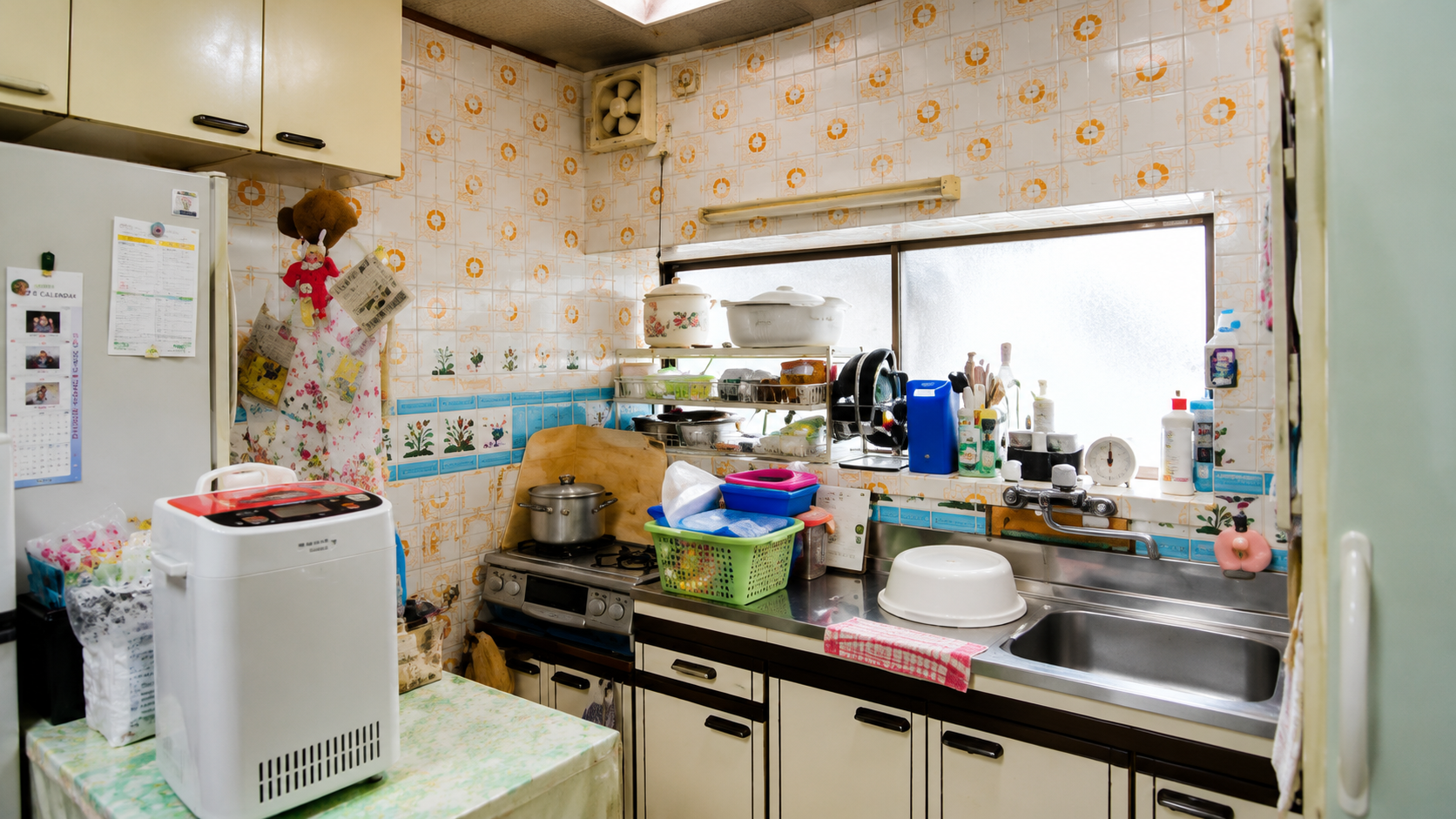 Small retro kitchen with tiled walls, a sink to the right, and a cluttered counter of pots, dishes, and a dish rack.
