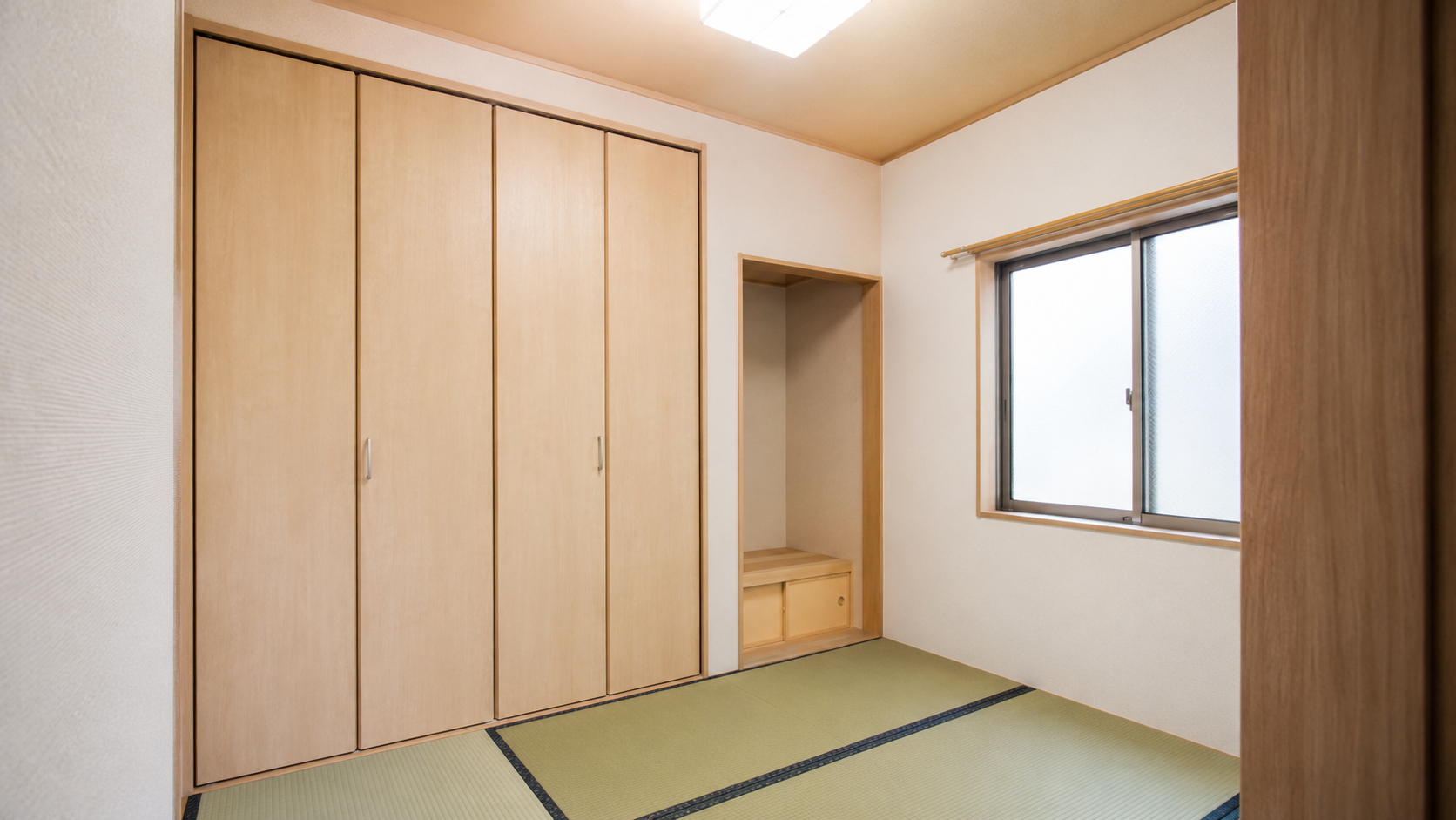 Japanese-style room with tatami mats, a row of tall wooden closets, and a small built-in alcove with a bench and drawers beside a frosted window