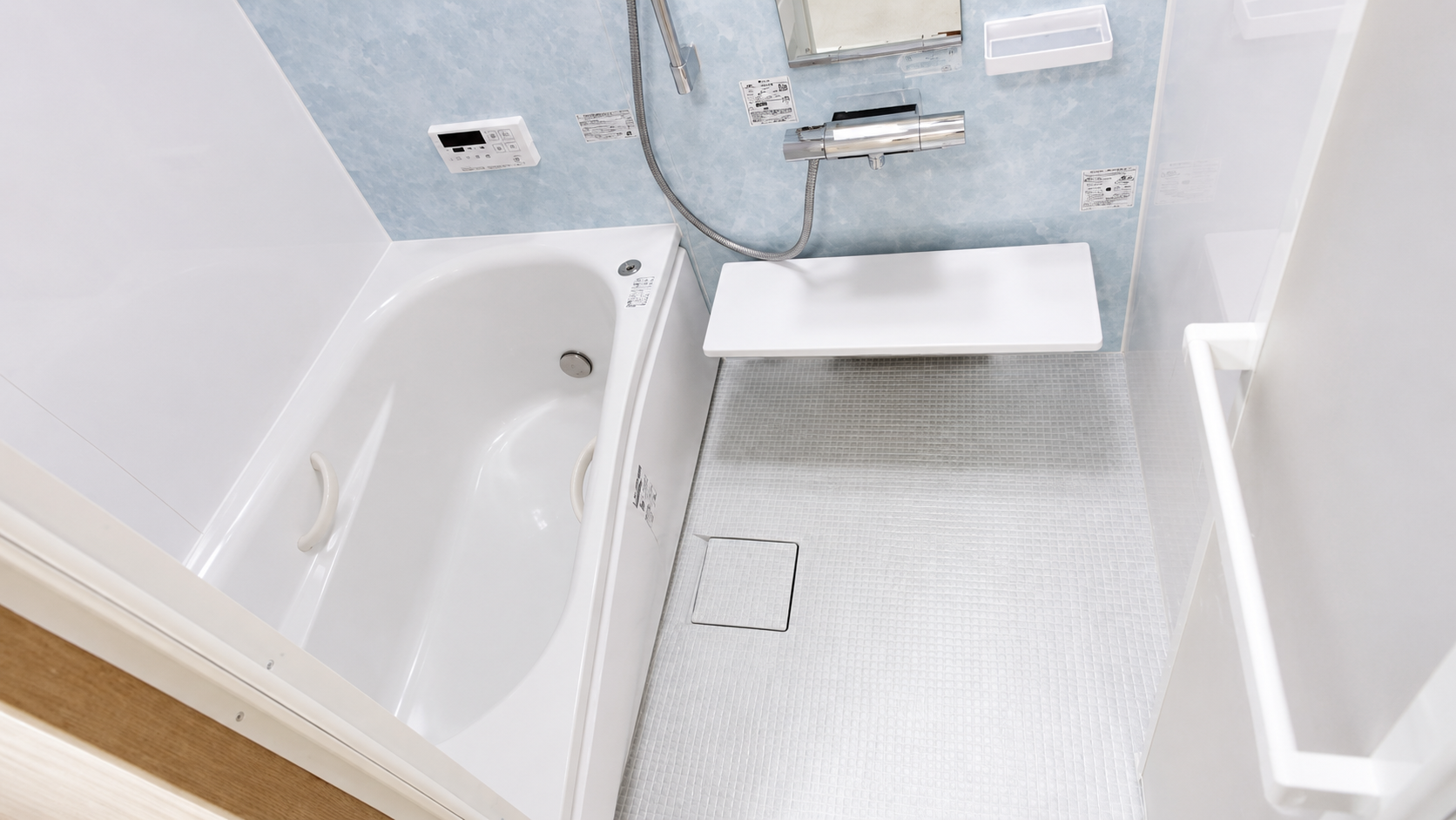 Compact bathroom with a white bathtub on the left, handheld shower, wall controls, and a small white bench against blue wall.