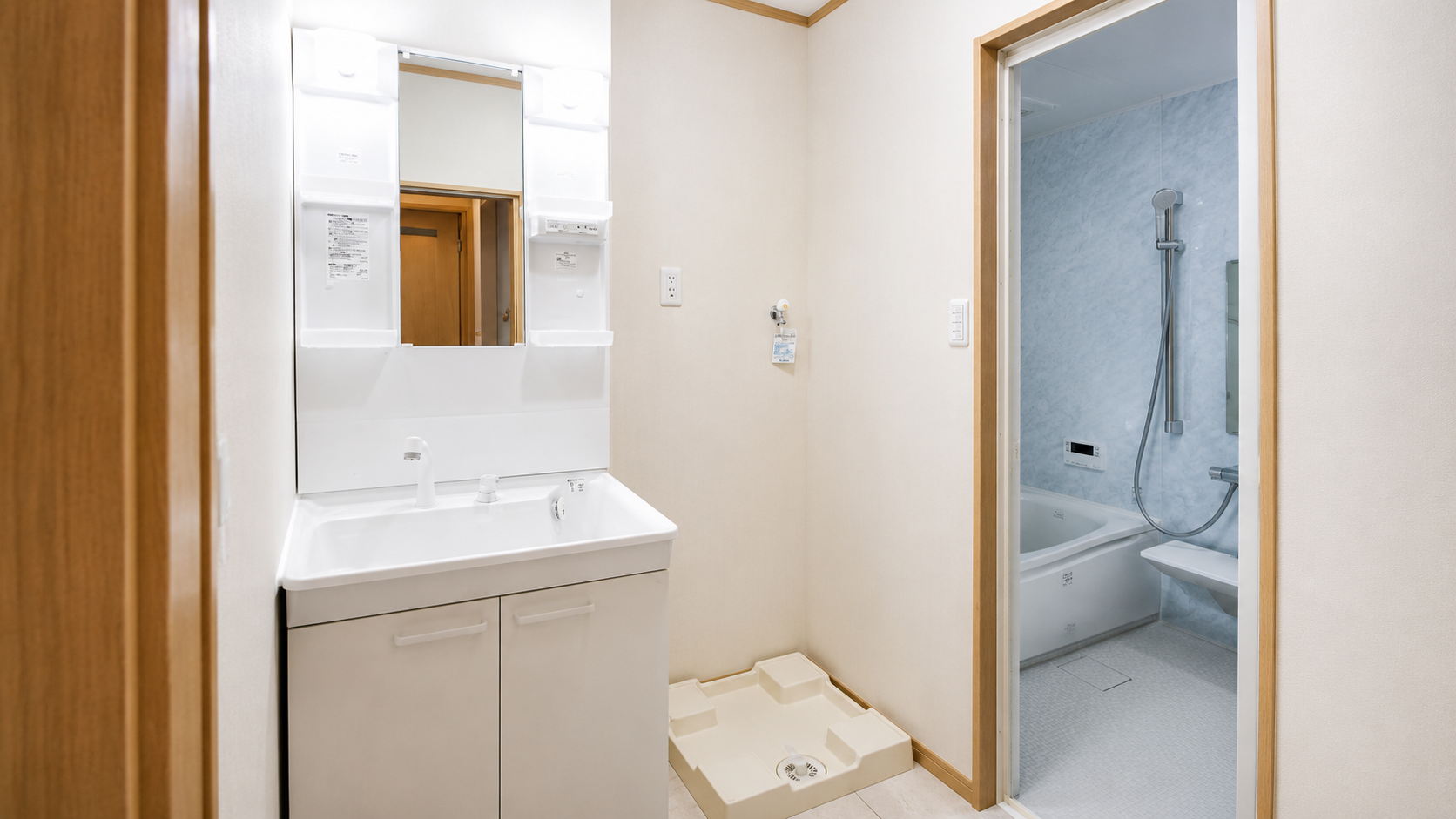 White bathroom vanity with sink and mirror, adjacent to an open doorway leading to a blue-tiled bath with a handheld shower.