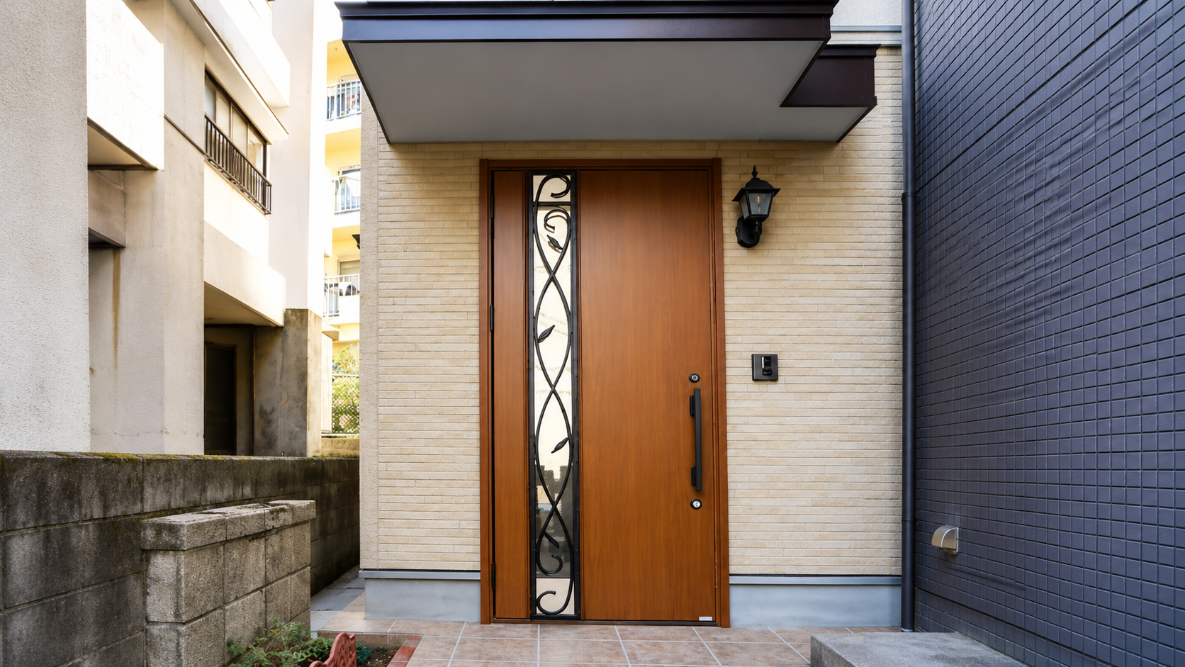 Wooden front door with decorative glass panel and wrought-iron scrollwork beside a beige brick entry, illuminated by a black exterior lantern.