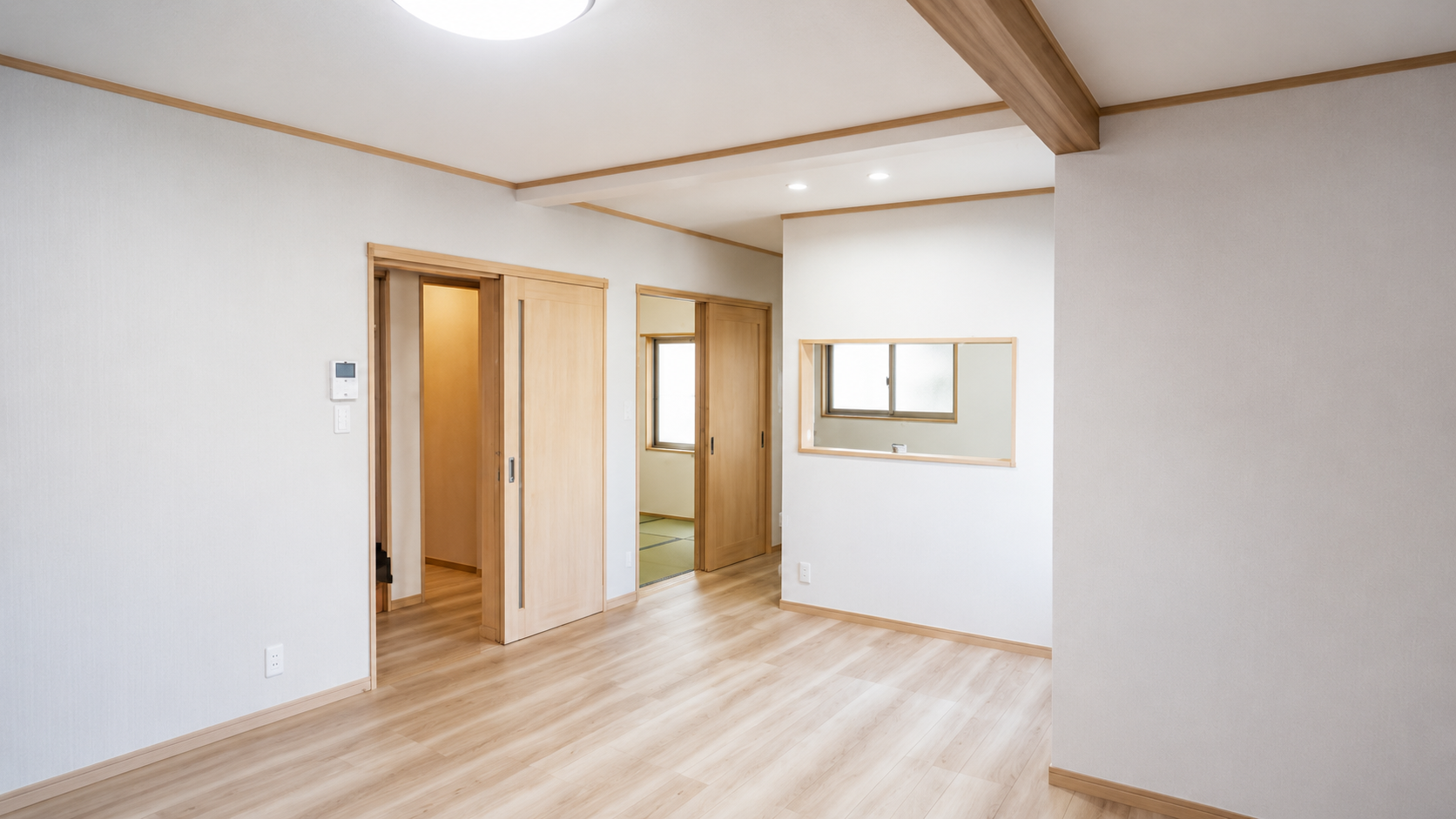 Bright interior living space with light wood floors, wooden trim, and sliding wooden doors along a hallway, plus a pass-through window in the wall