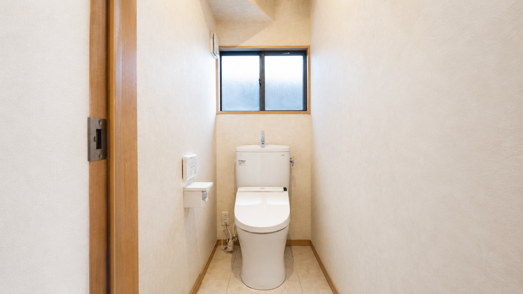 Narrow bathroom with a white modern toilet and control panel on the left, frosted window above the toilet.