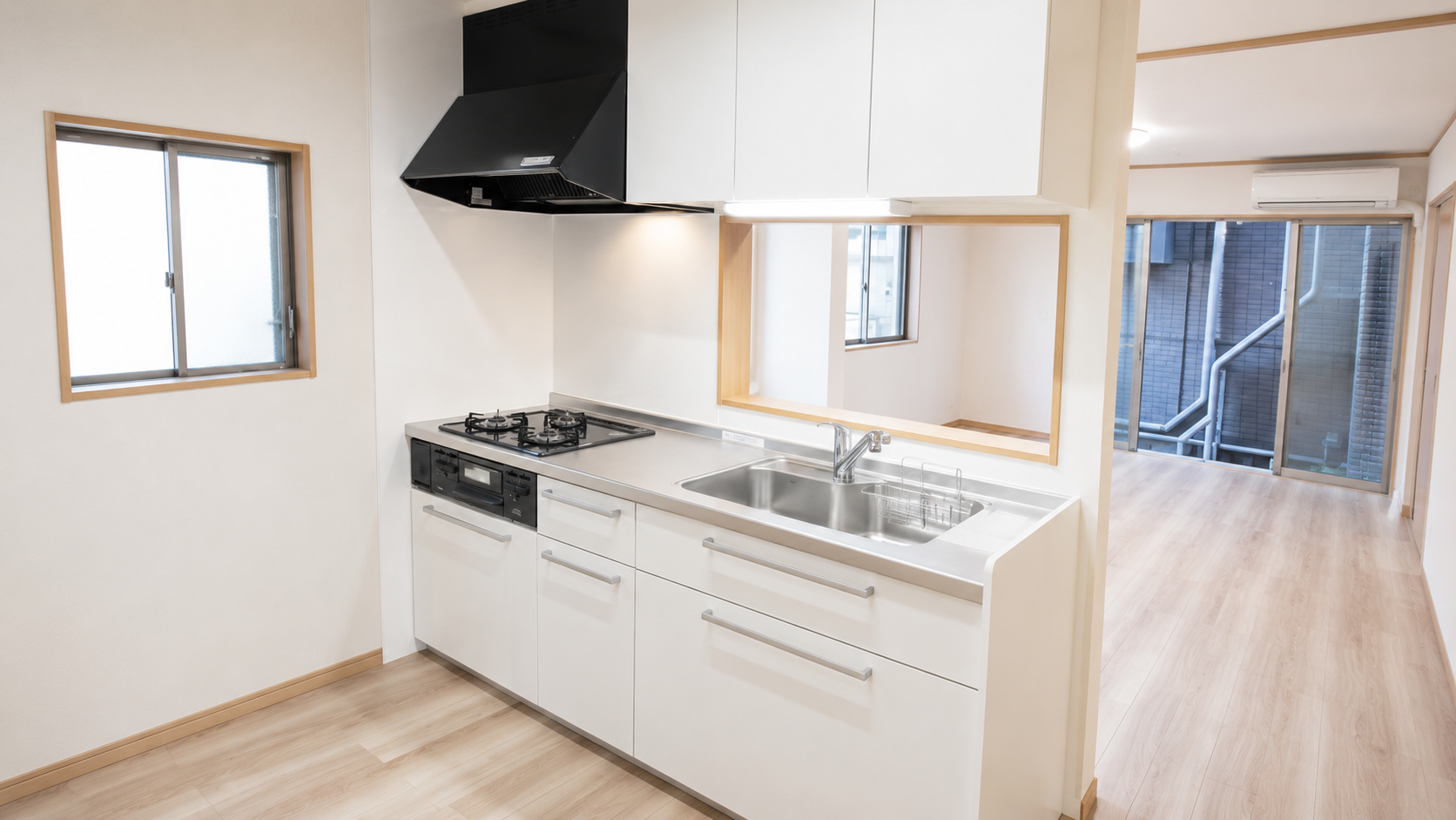 Modern kitchen with white cabinets, stainless steel counter, gas stove, and sink; open plan to living area with large windows and light wood flooring