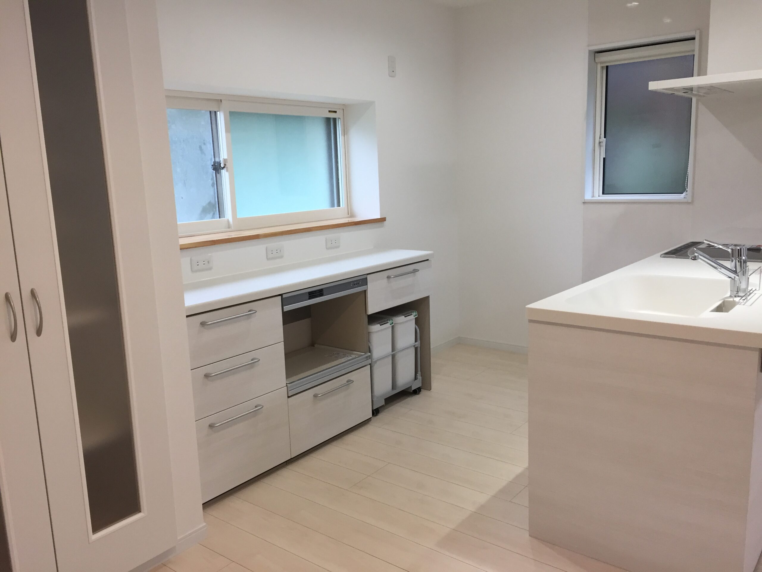 Bright white kitchen with an island, sink, built-in oven, and two frosted windows.