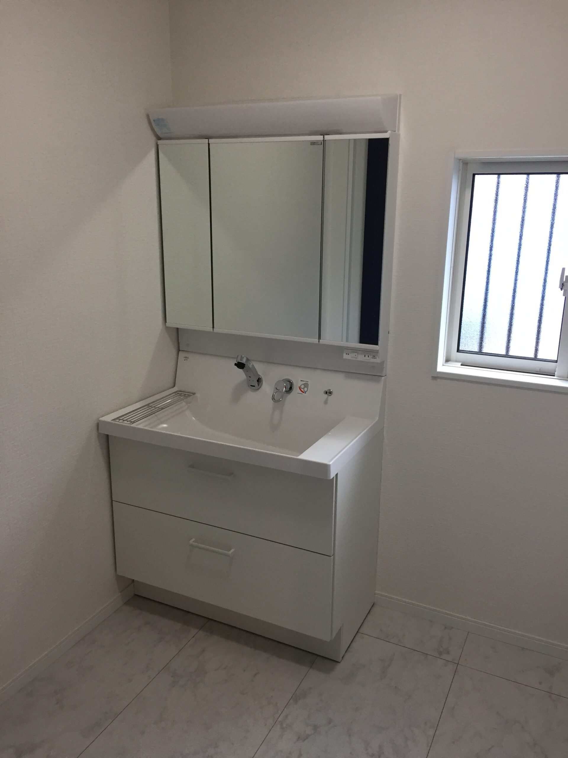White bathroom vanity with integrated sink and mirrored cabinet above, near a small window; minimalist, clean look.