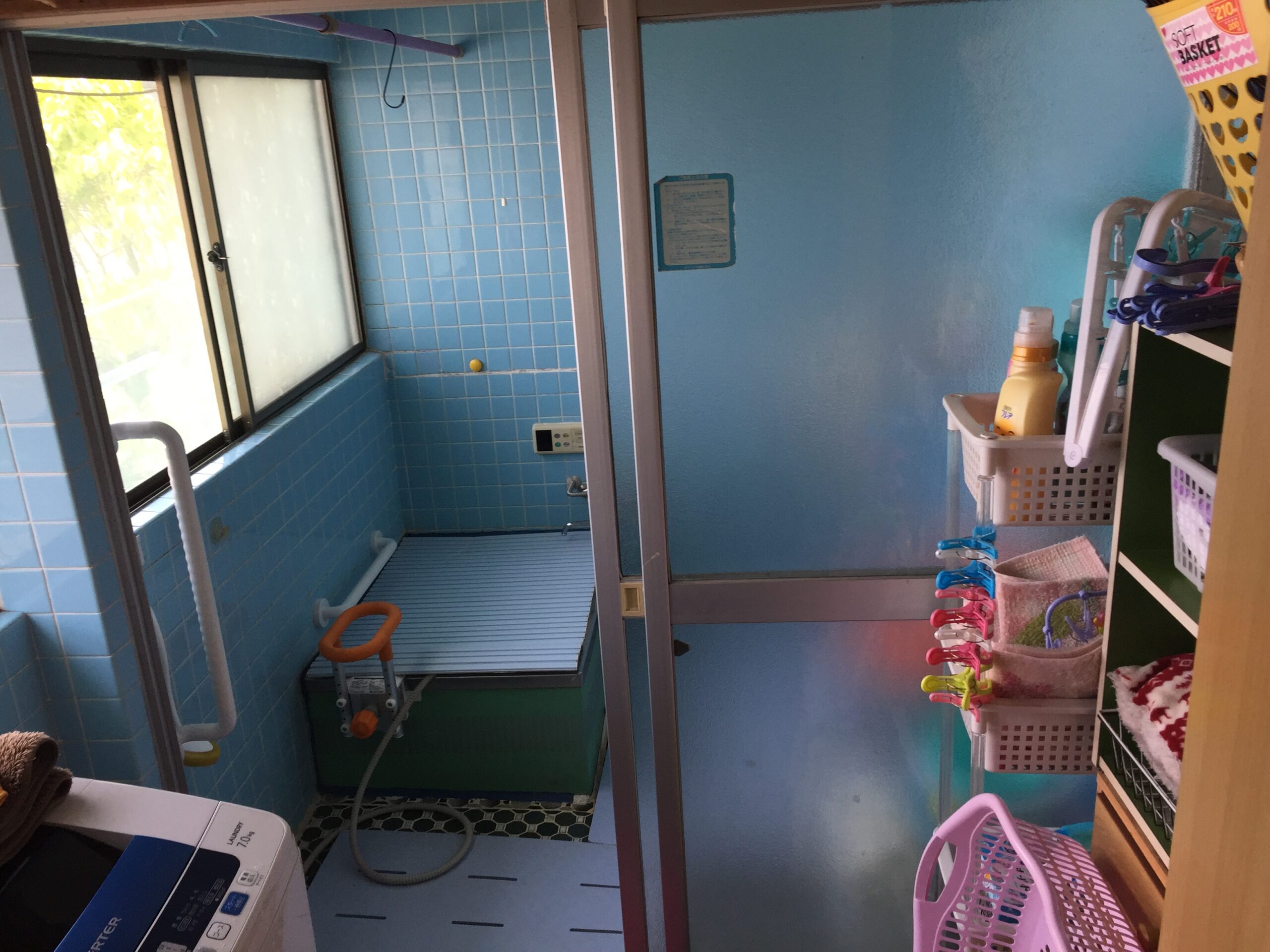 Blue tiled bathroom/laundry area with a glass door, washing machine in the foreground, and blue-tiled walls on the left side.