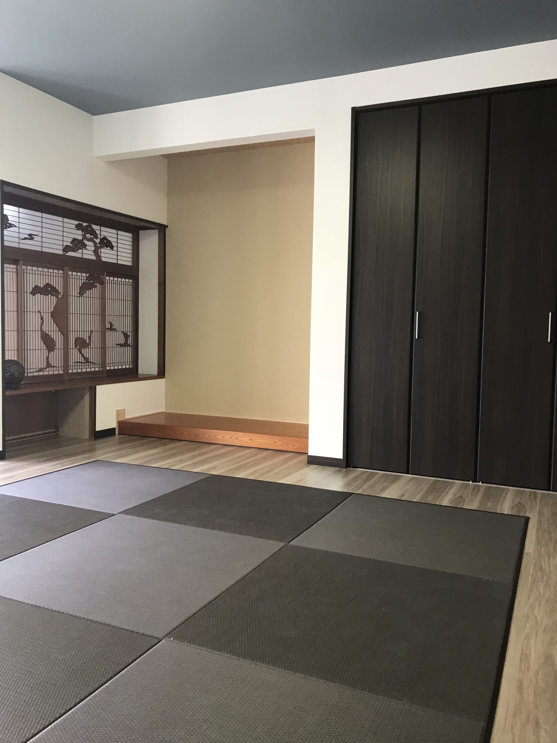 Japanese-style room with tatami mats, dark wood closet on the right, and an alcove with a decorative screen featuring a tree motif