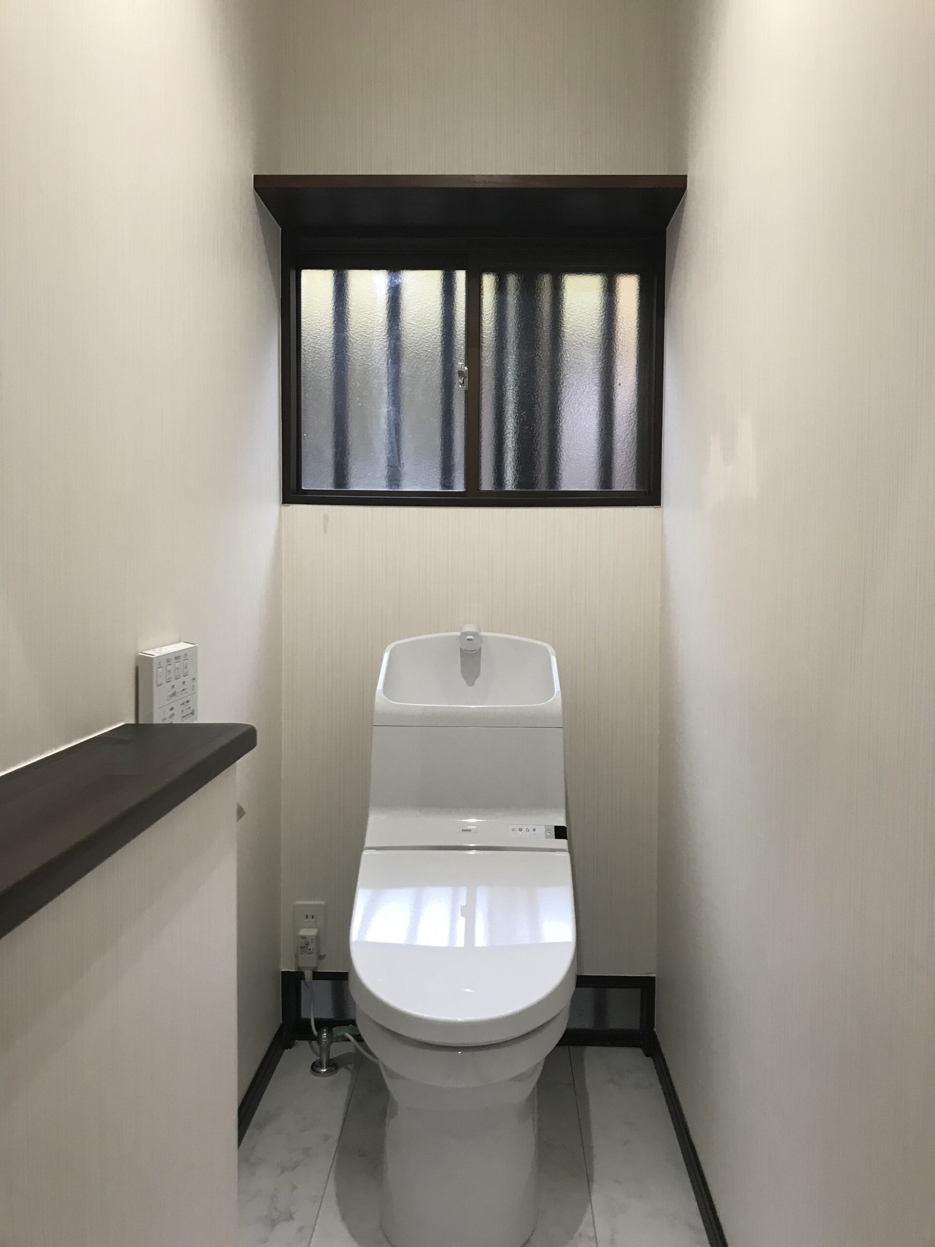 Narrow bathroom with a white modern toilet beneath a frosted window and dark trim.