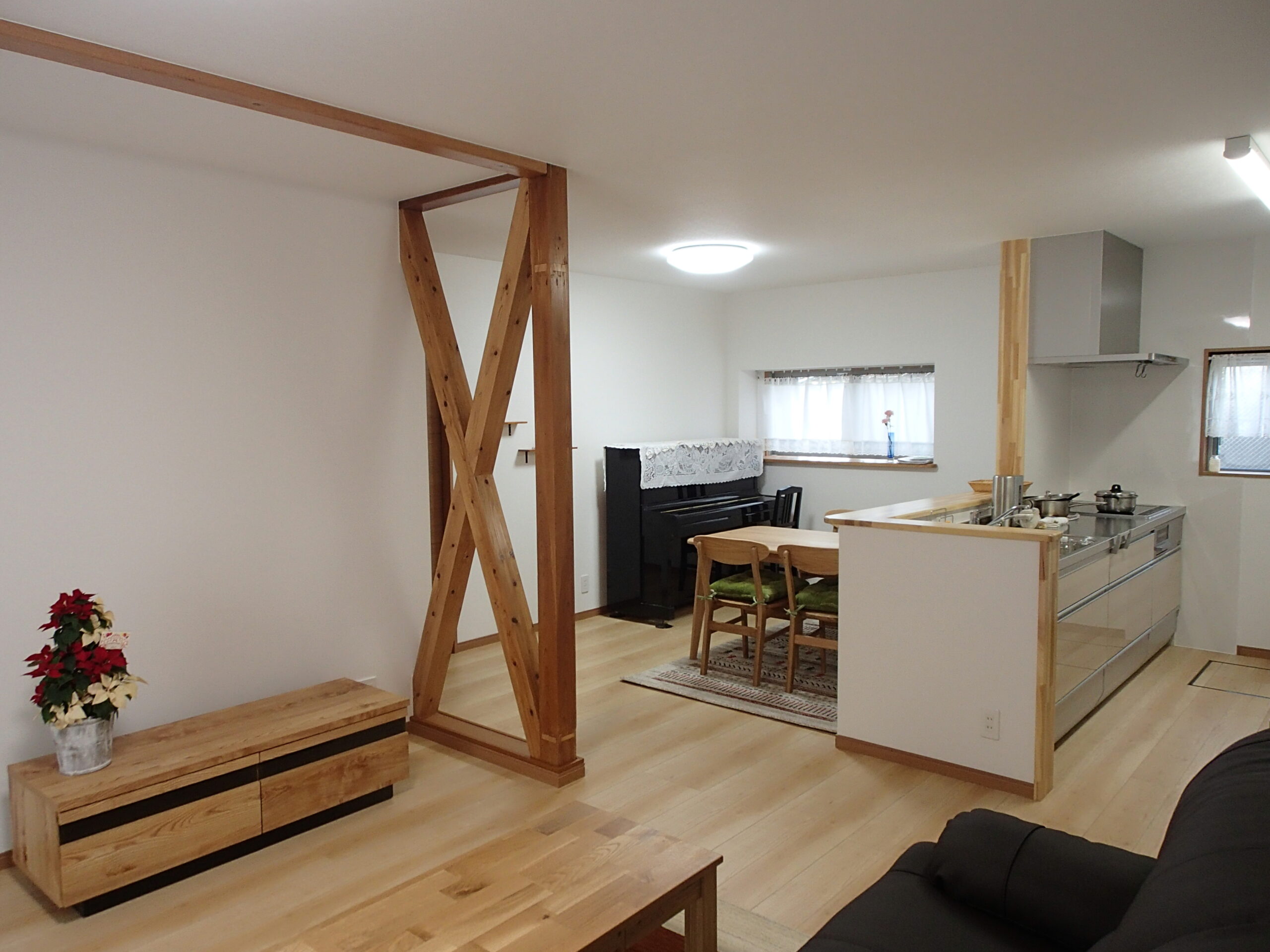 Open-concept living area featuring a wooden diagonal beam divider, a piano against the back wall, and a kitchen with an island on the right.