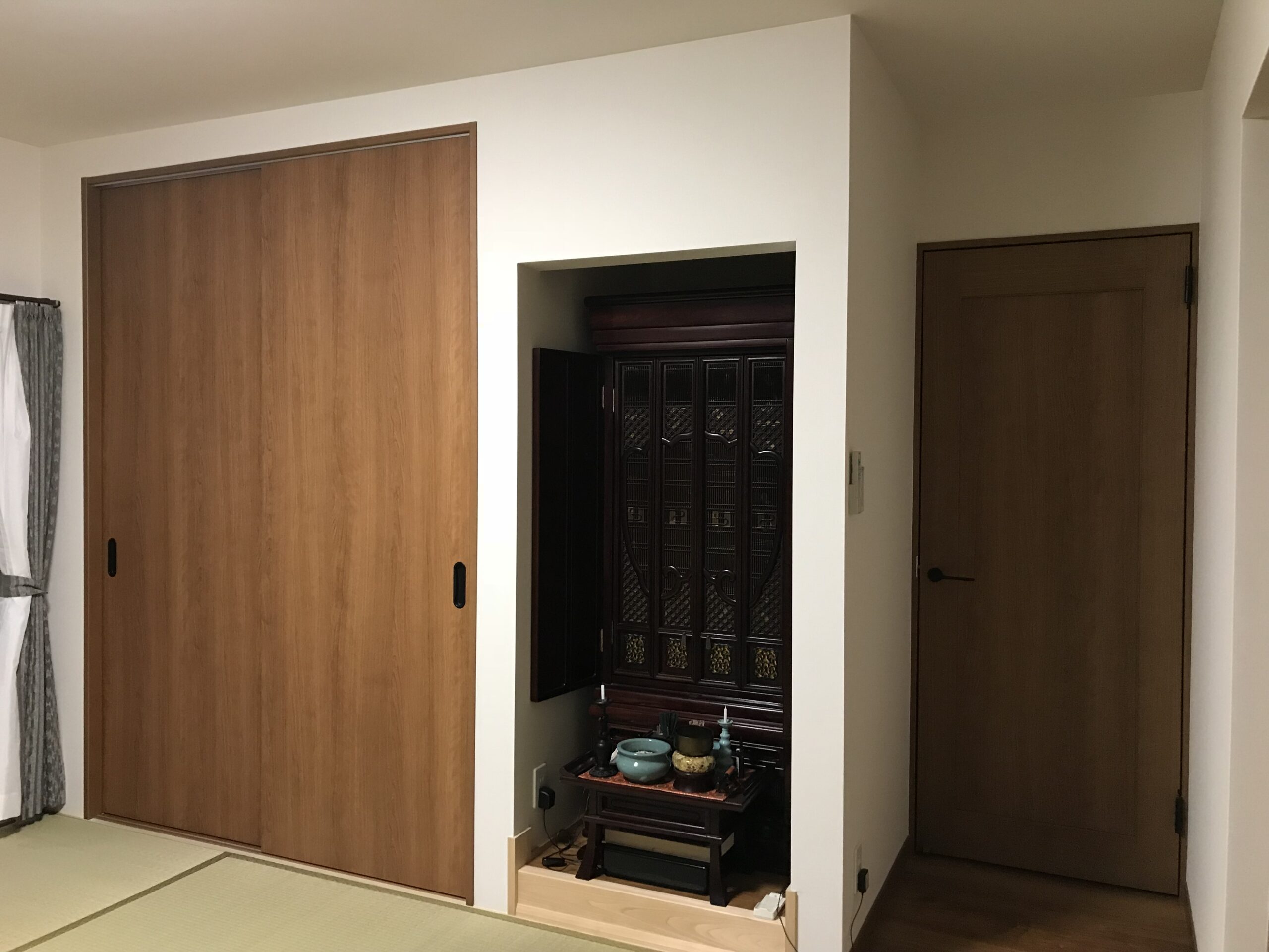 Interior hallway with large wooden sliding doors; a decorative alcove houses a dark ornate altar or cabinet centerpiece.