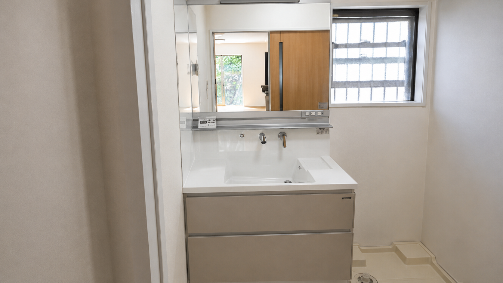 Modern bathroom vanity with a white sink, gray drawers, and a large mirror above; a window to the right adds natural light.