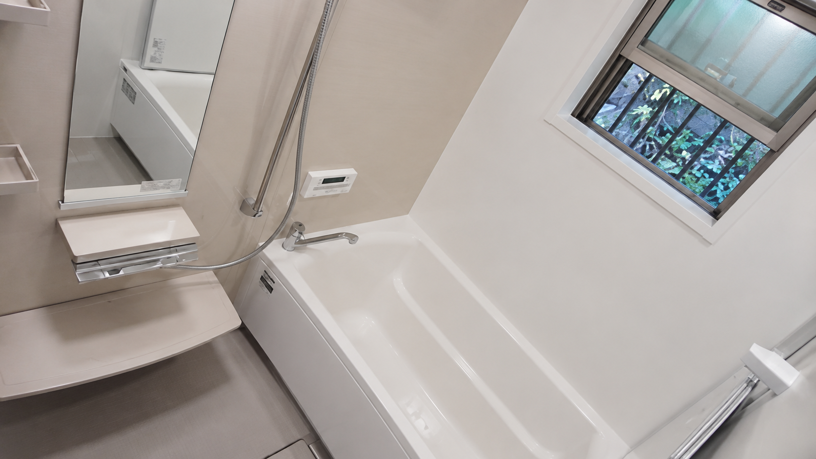 Modern bathroom with a white rectangular bathtub, handheld shower, and large mirror; window with greenery outside.