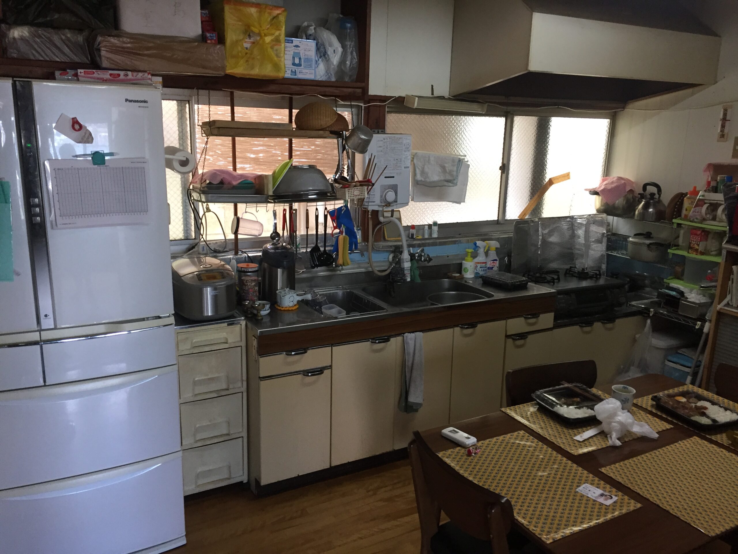Cluttered home kitchen with a refrigerator, sink, dish rack, and hanging utensils on a central rack.