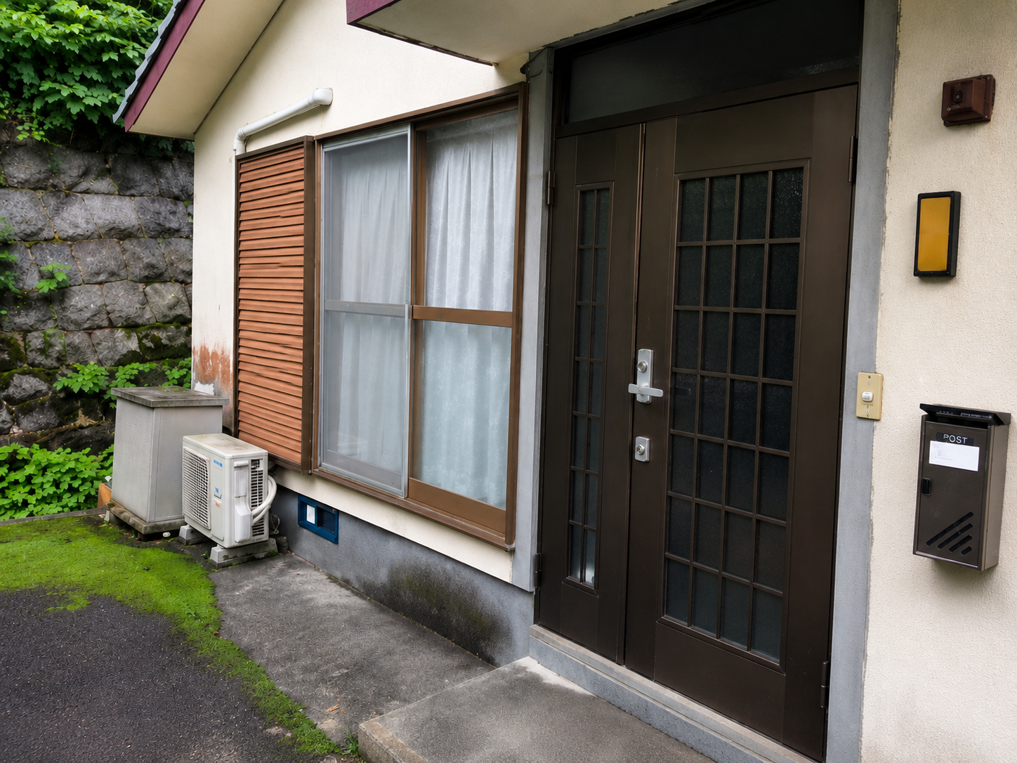 Residential entrance with a dark brown door featuring grid glass panels and a large window with brown shutters beside it.