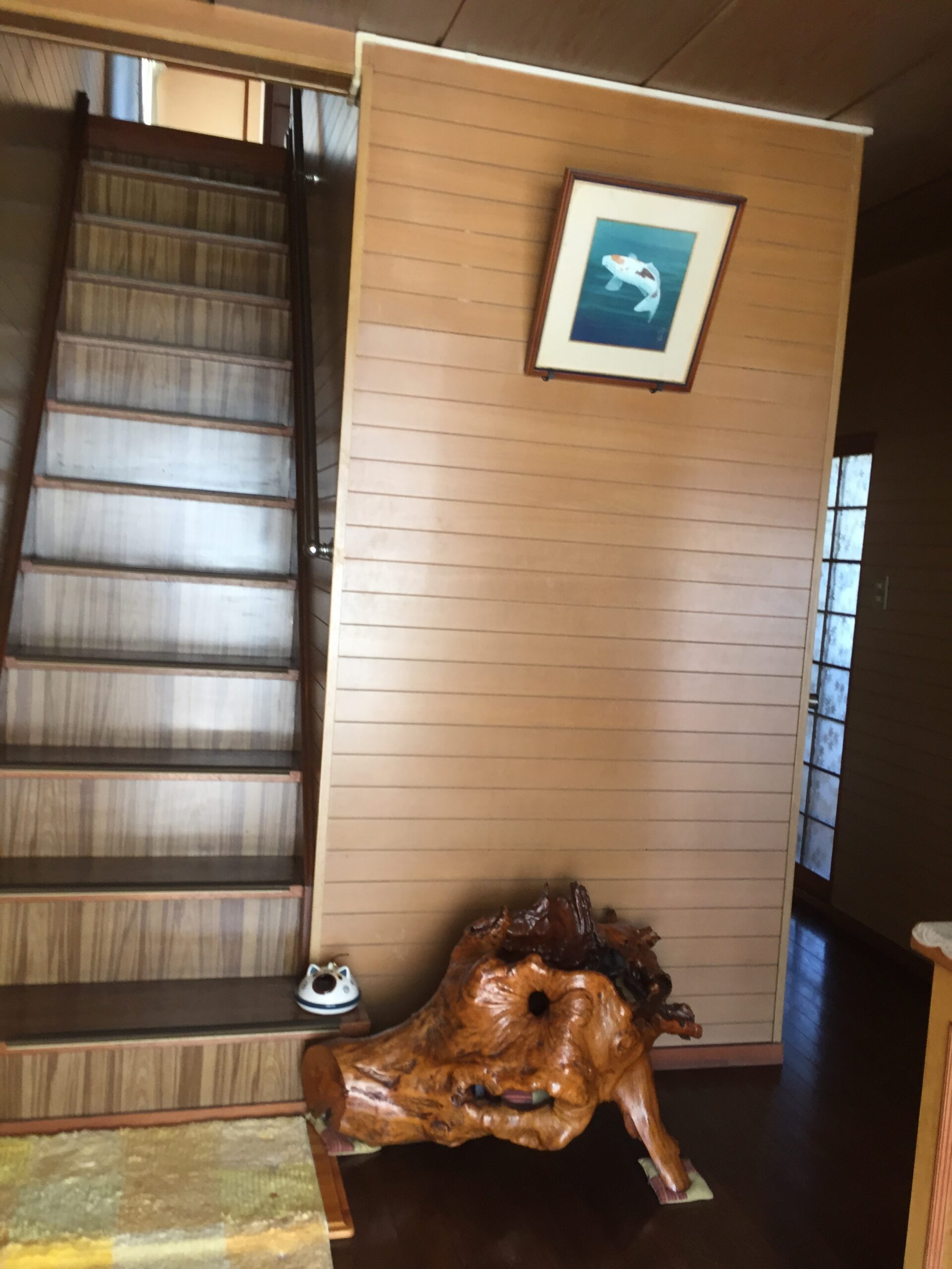 Paneled hallway scene with a framed koi fish painting on the wall and a large carved wooden sculpture on the floor next to stairs.